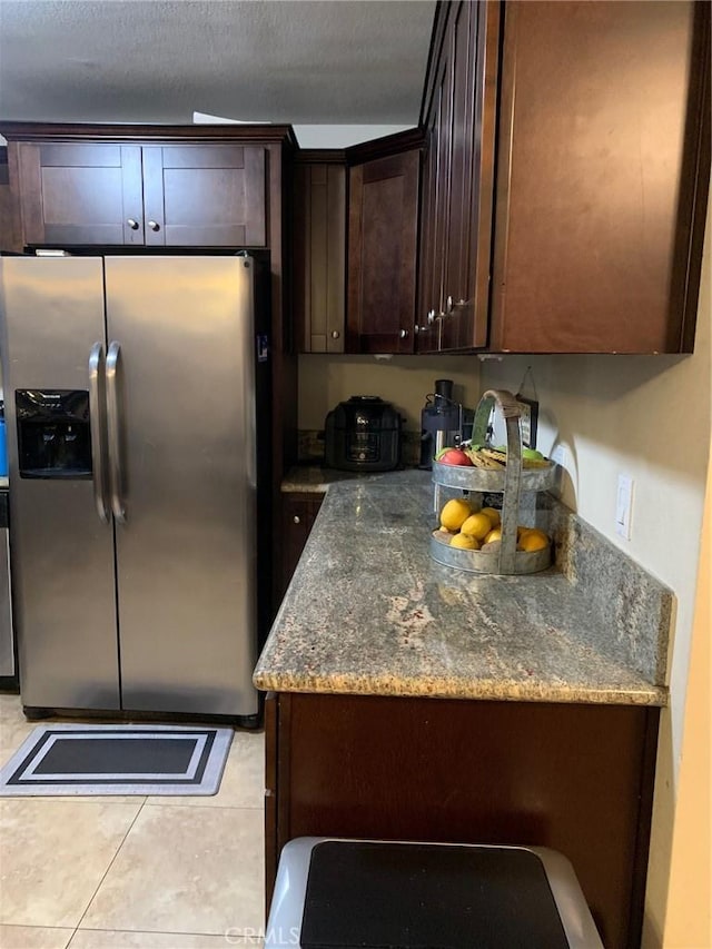 kitchen with light tile patterned floors, stone countertops, dark brown cabinetry, stainless steel refrigerator with ice dispenser, and a textured ceiling