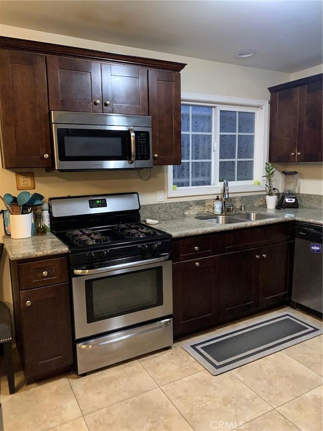 kitchen with dark brown cabinetry, light tile patterned flooring, appliances with stainless steel finishes, and a sink