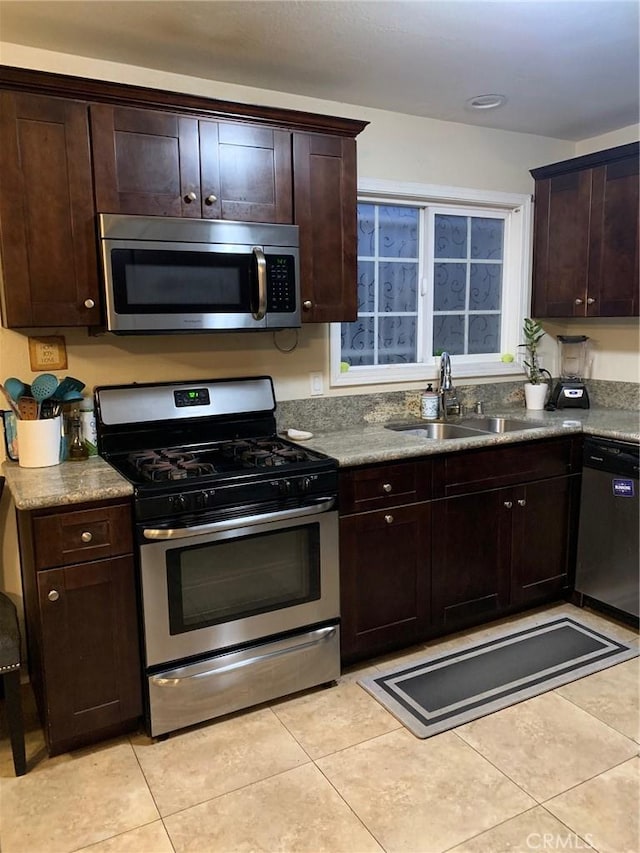 kitchen with dark brown cabinetry, light tile patterned floors, appliances with stainless steel finishes, and a sink