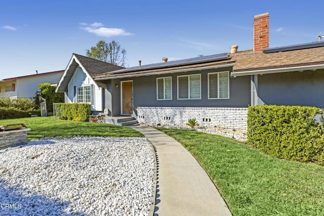 ranch-style house with a shingled roof, a front yard, roof mounted solar panels, stucco siding, and crawl space