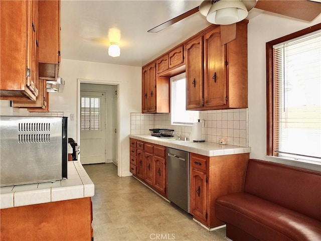 kitchen with stainless steel dishwasher, tile countertops, brown cabinets, and backsplash