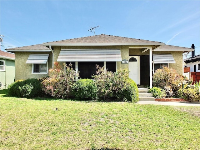 view of front of home featuring stucco siding, a shingled roof, and a front yard