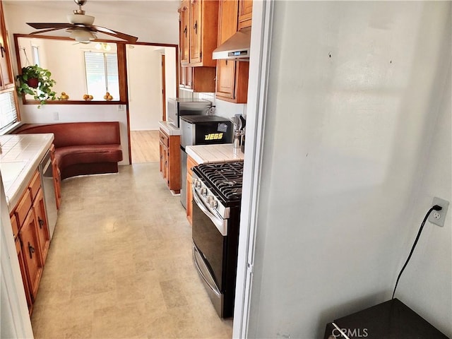 kitchen featuring tile countertops, stainless steel appliances, brown cabinets, and under cabinet range hood