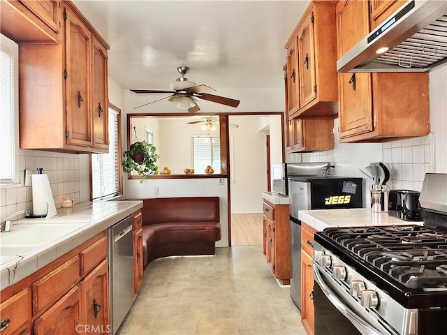 kitchen featuring tile countertops, appliances with stainless steel finishes, brown cabinets, and under cabinet range hood