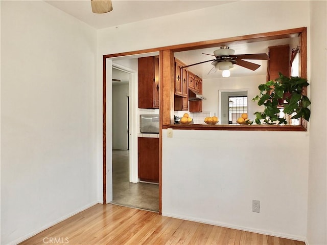 kitchen featuring light wood finished floors, decorative backsplash, under cabinet range hood, and ceiling fan