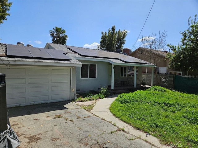 ranch-style house with driveway, a porch, a garage, roof mounted solar panels, and stucco siding