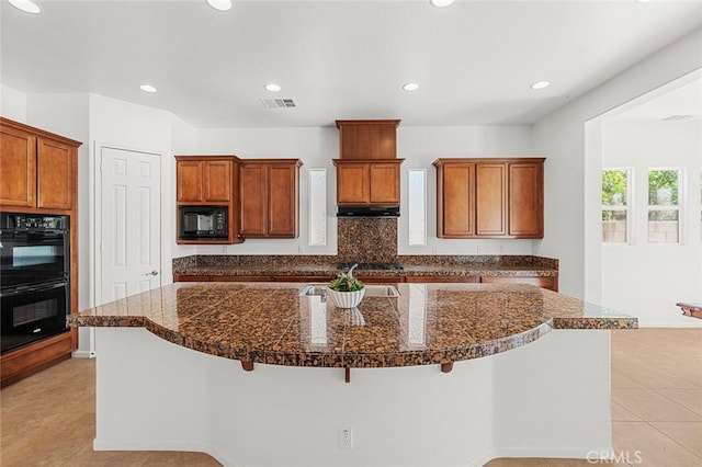 kitchen with visible vents, a kitchen bar, light tile patterned floors, brown cabinetry, and black appliances