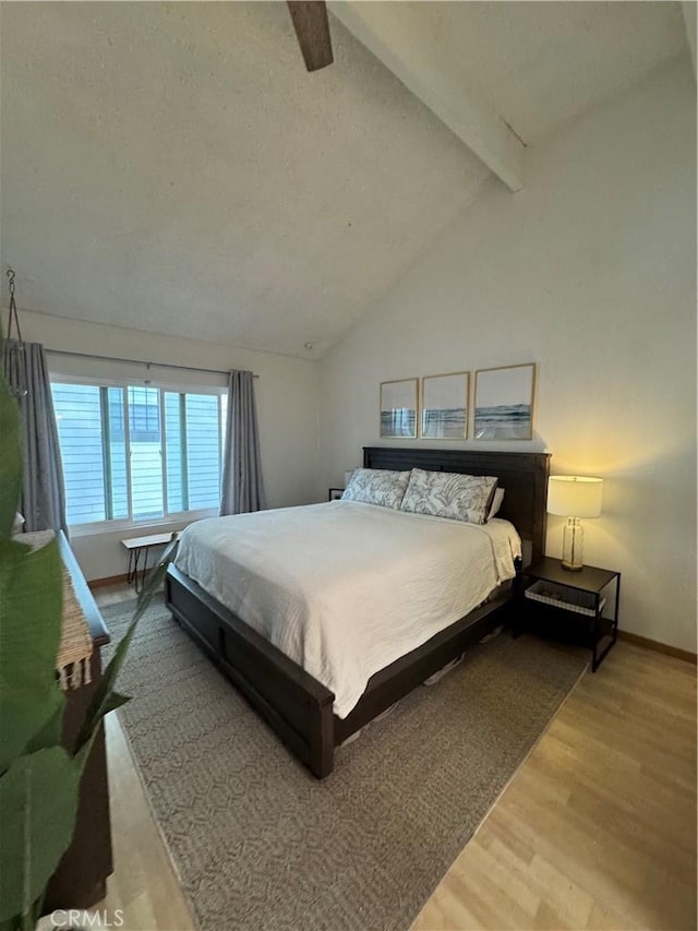 bedroom featuring lofted ceiling with beams, wood finished floors, and baseboards