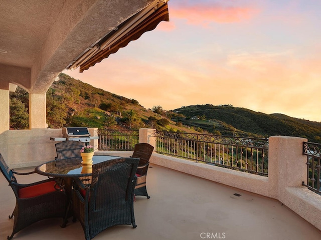 patio terrace at dusk with a mountain view, outdoor dining area, and a balcony