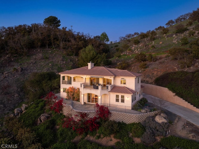 back of property with driveway, a tile roof, fence, a balcony, and a chimney