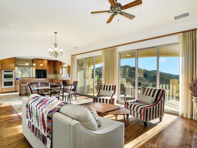 living room with a mountain view, ceiling fan with notable chandelier, visible vents, and light wood finished floors