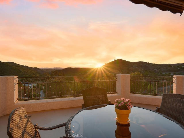 patio terrace at dusk with a balcony, outdoor dining area, and a mountain view