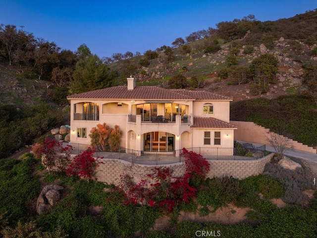 rear view of property featuring a balcony, fence, stucco siding, a chimney, and a tiled roof