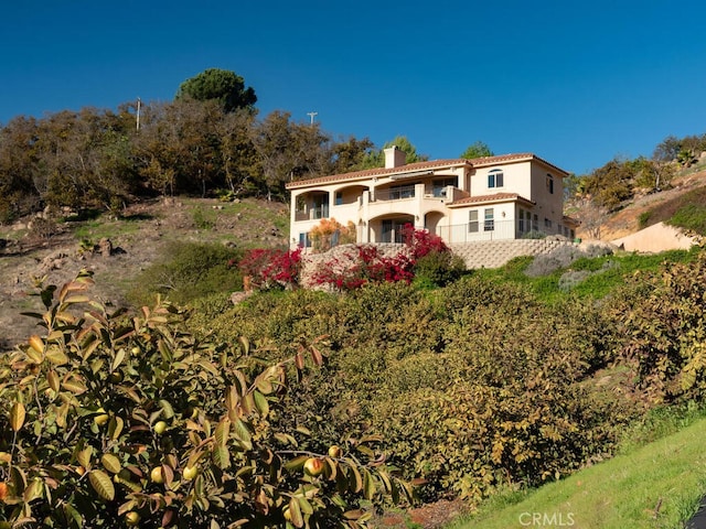 view of front of property with stucco siding, a balcony, a tile roof, and a chimney