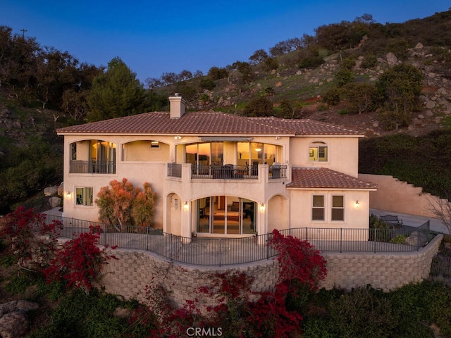 rear view of house with a balcony, fence, stucco siding, a chimney, and a patio area