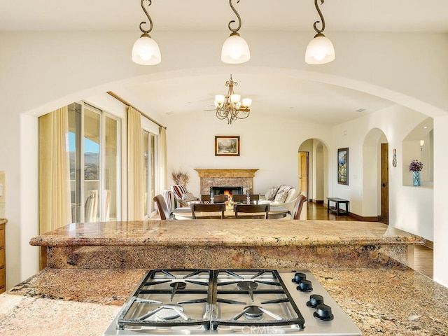 kitchen with vaulted ceiling, decorative light fixtures, stainless steel gas cooktop, and a lit fireplace