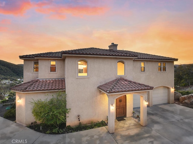 mediterranean / spanish-style home featuring stucco siding, concrete driveway, a chimney, and a tile roof