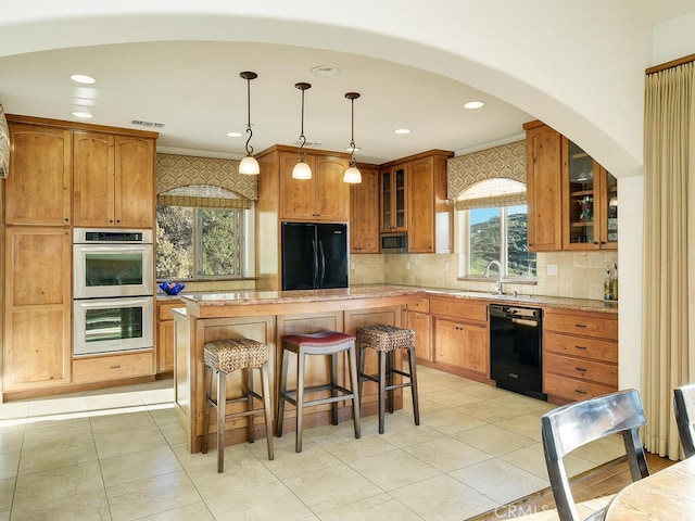 kitchen with black appliances, glass insert cabinets, a kitchen breakfast bar, brown cabinets, and a center island