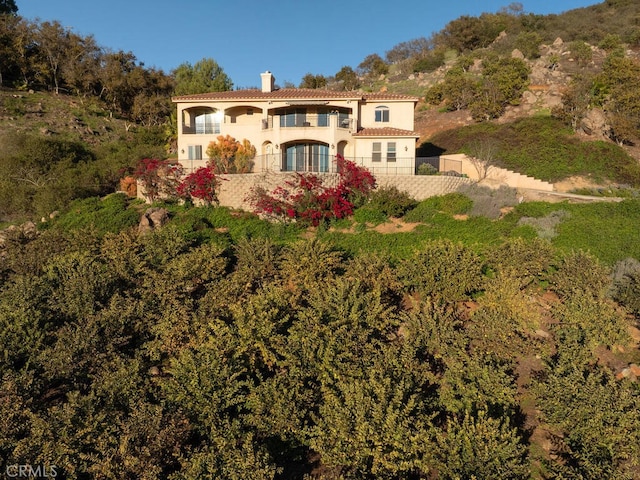 view of front of home with stucco siding, a chimney, a balcony, and fence