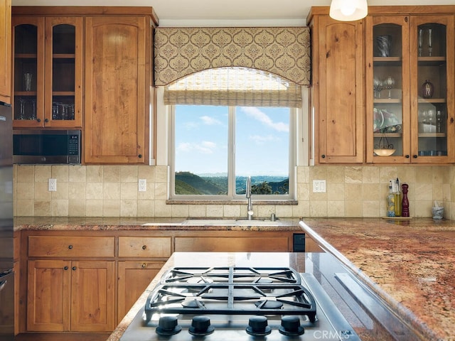 kitchen featuring a sink, stainless steel appliances, glass insert cabinets, and brown cabinetry