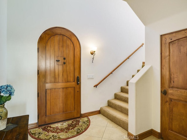 foyer featuring light tile patterned flooring, stairway, arched walkways, and baseboards