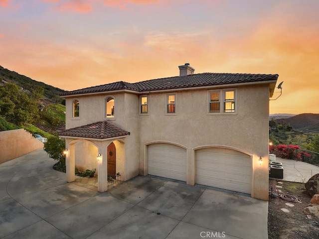 mediterranean / spanish-style house with a chimney, stucco siding, concrete driveway, and a tile roof