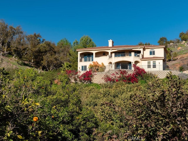 mediterranean / spanish home with stucco siding, a balcony, and a chimney