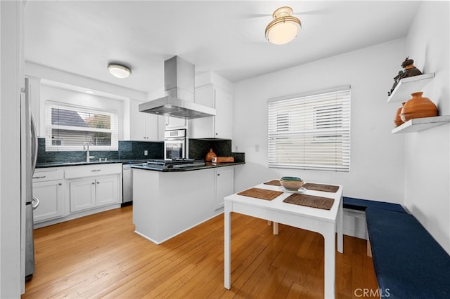 kitchen featuring tasteful backsplash, light wood finished floors, white cabinets, wall chimney exhaust hood, and a sink