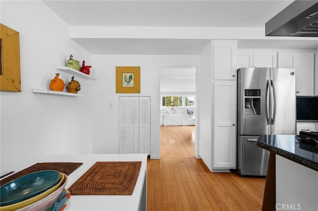 kitchen with light wood finished floors, stainless steel fridge, white cabinetry, and wall chimney range hood