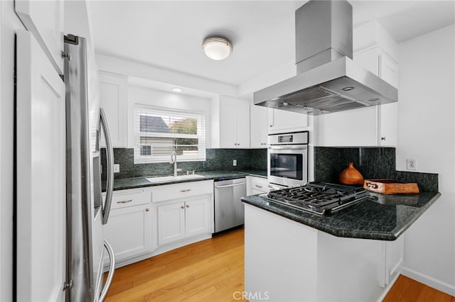 kitchen featuring appliances with stainless steel finishes, a peninsula, island range hood, white cabinets, and a sink