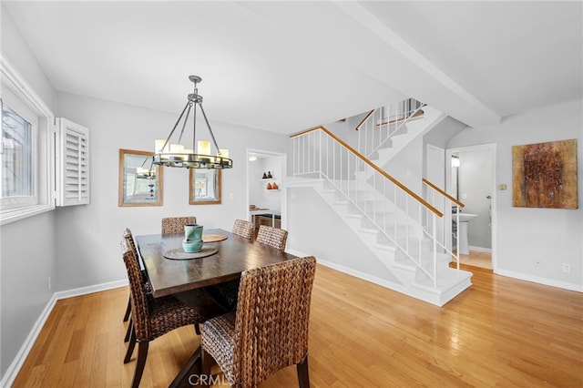 dining room featuring a notable chandelier, baseboards, stairs, and light wood-style floors