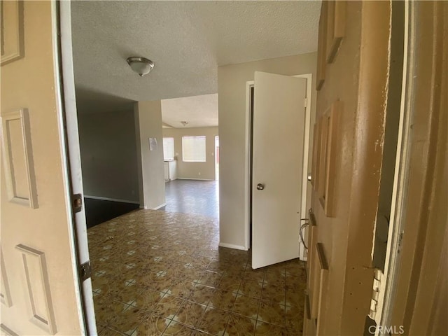 corridor with a textured ceiling and baseboards