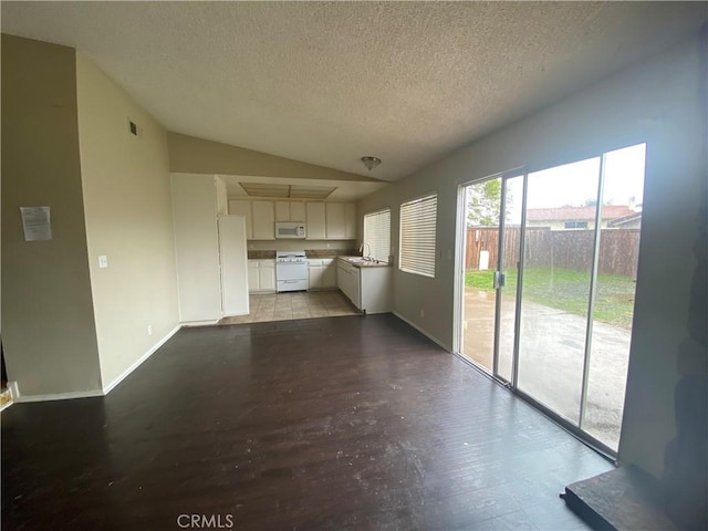 unfurnished living room with lofted ceiling, a sink, a textured ceiling, wood finished floors, and baseboards