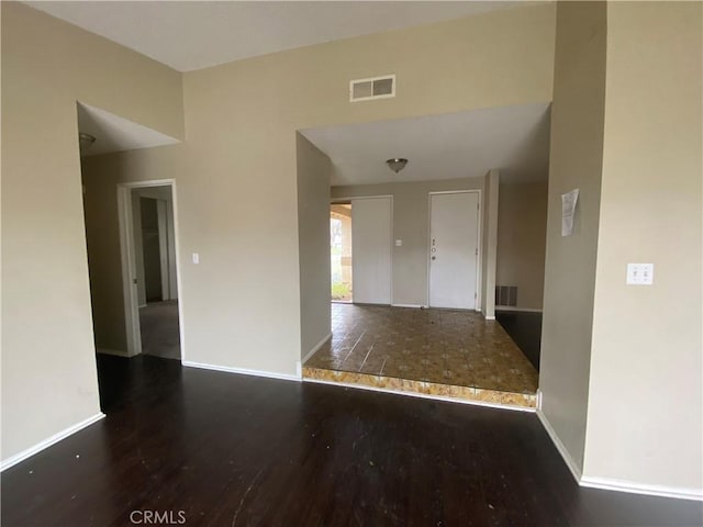 empty room featuring wood finished floors, visible vents, and baseboards