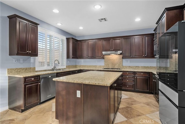 kitchen with a center island, under cabinet range hood, stainless steel dishwasher, light stone counters, and dark brown cabinets