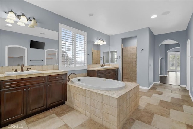 bathroom with two vanities, a bath, a walk in shower, and a sink