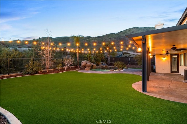 view of yard featuring a ceiling fan, a fenced backyard, a mountain view, and a patio