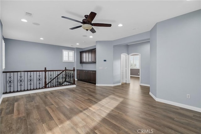 spare room featuring wood finished floors, arched walkways, baseboards, and ceiling fan