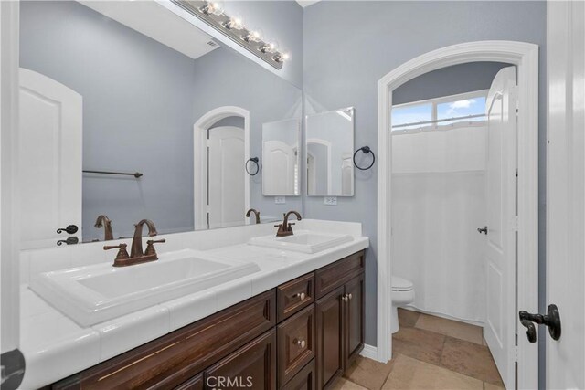 full bathroom with double vanity, a shower with shower curtain, toilet, and a sink