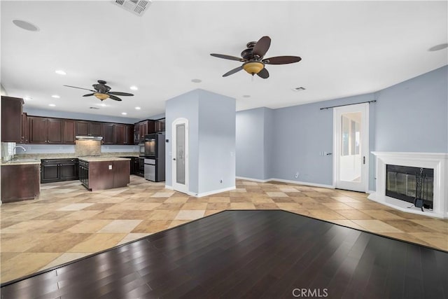 kitchen featuring visible vents, a kitchen island, a ceiling fan, dark brown cabinetry, and a sink