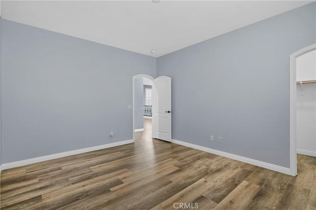 empty room featuring arched walkways, baseboards, and wood finished floors