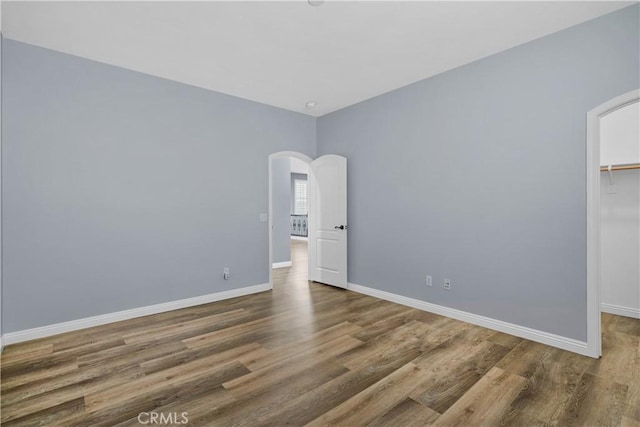 unfurnished room featuring arched walkways, baseboards, and wood finished floors