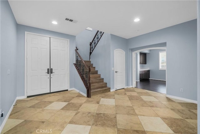 entrance foyer featuring stairway, arched walkways, visible vents, and baseboards