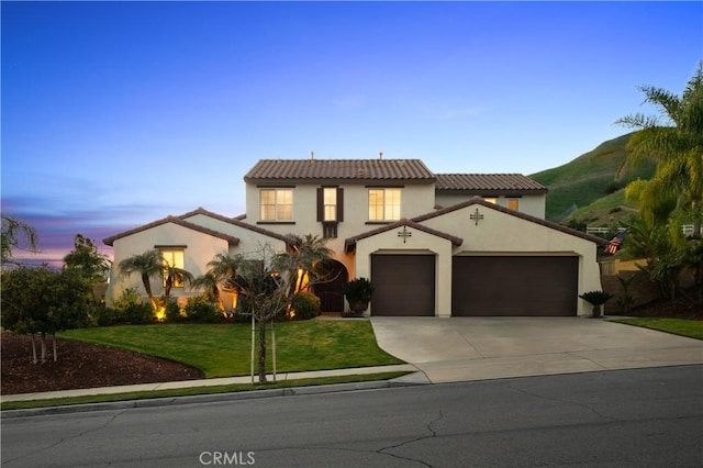 mediterranean / spanish-style home with a garage, stucco siding, a tile roof, a front lawn, and driveway