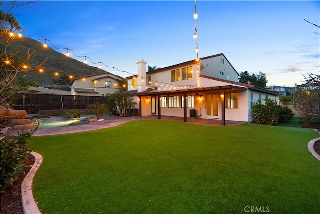 back of property at dusk with a patio, a yard, fence, and stucco siding