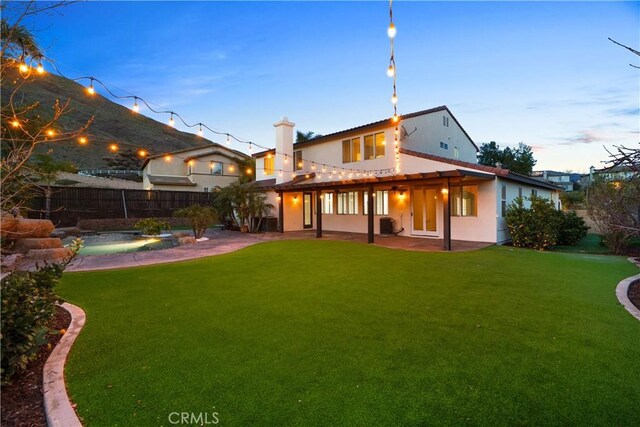 rear view of property featuring fence, a lawn, stucco siding, and a patio area