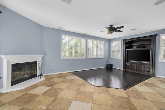 unfurnished living room featuring a glass covered fireplace, baseboards, visible vents, and ceiling fan