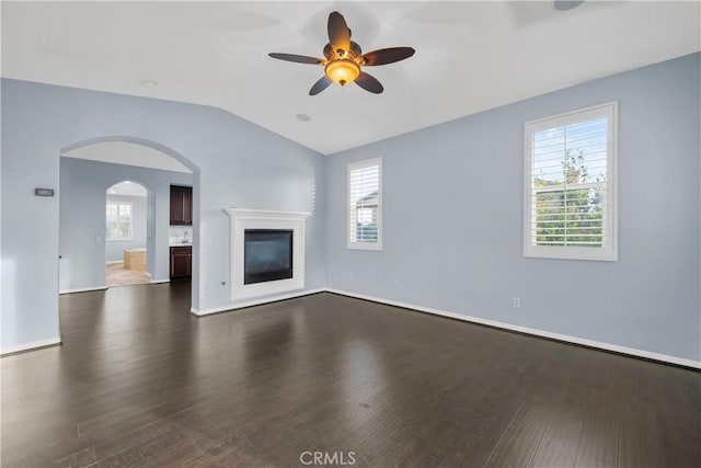 unfurnished living room with a ceiling fan, a glass covered fireplace, dark wood finished floors, arched walkways, and vaulted ceiling