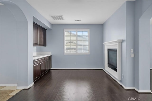 unfurnished living room with a glass covered fireplace, visible vents, and dark wood finished floors