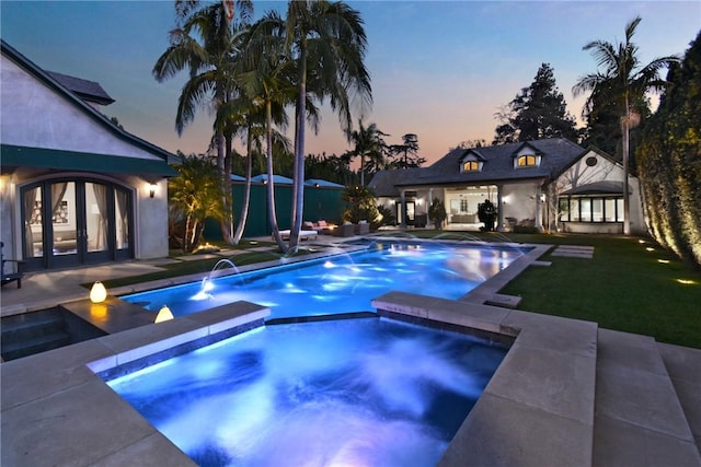 pool at dusk with a patio, a lawn, and a pool with connected hot tub